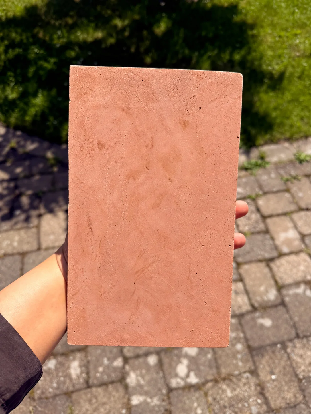 A Rumett Rosso Sand sample held in daylight, showing the cast variation across its face
